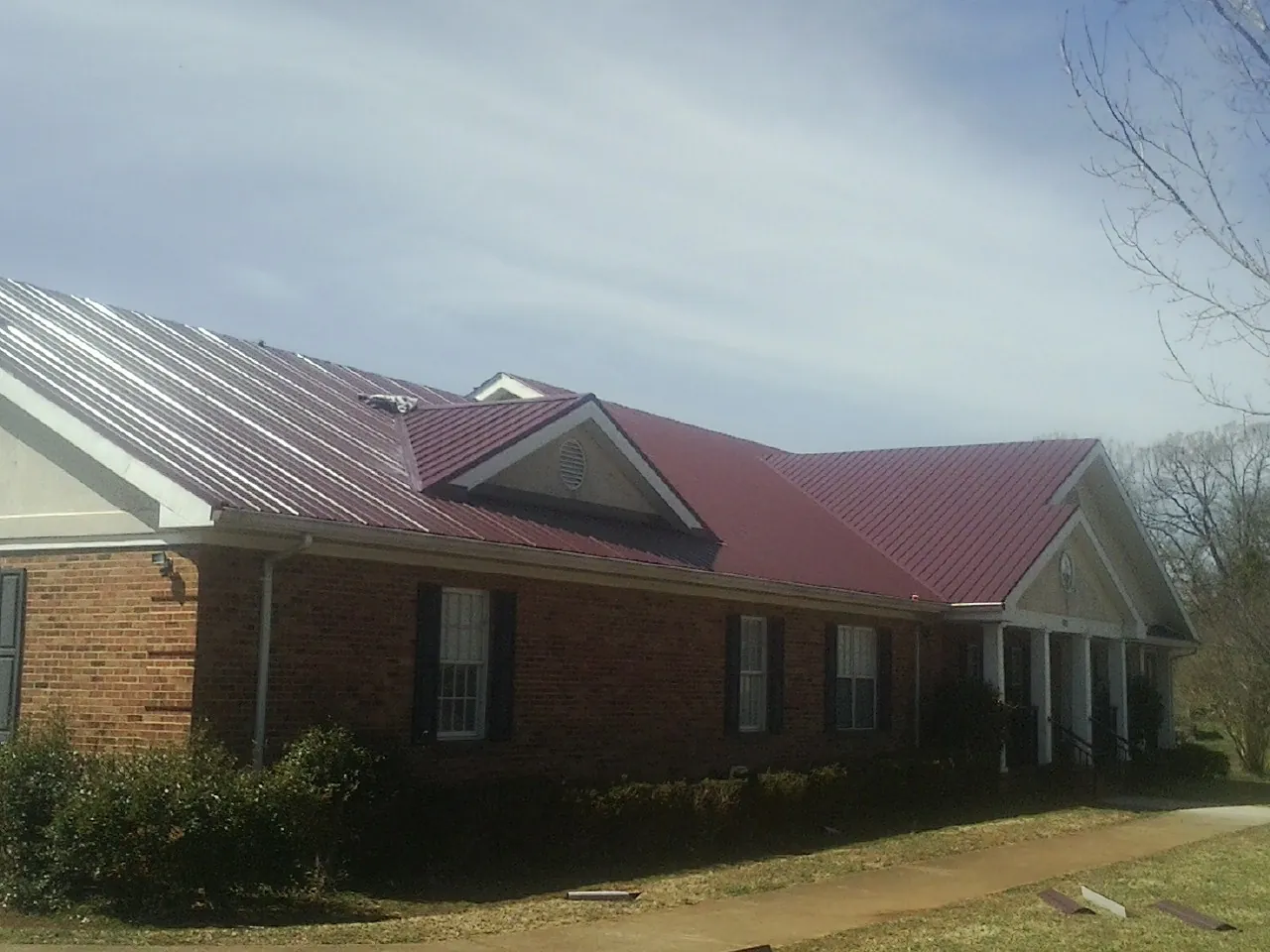 Red metal roof with gabled entries on a long brick building, from a Hail Damage Roof Repair job in Webster