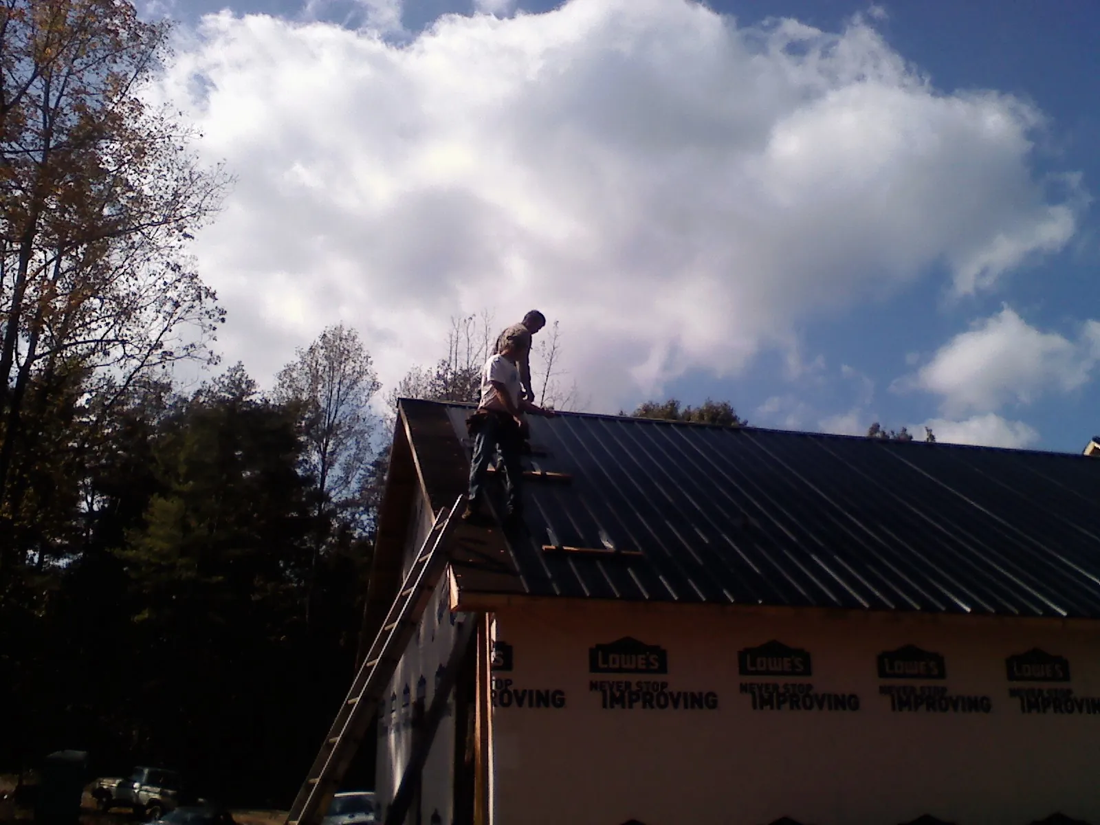 Roofer fastening dark metal panels high against a cloudy sky, from a Roof Inspection job in Webster